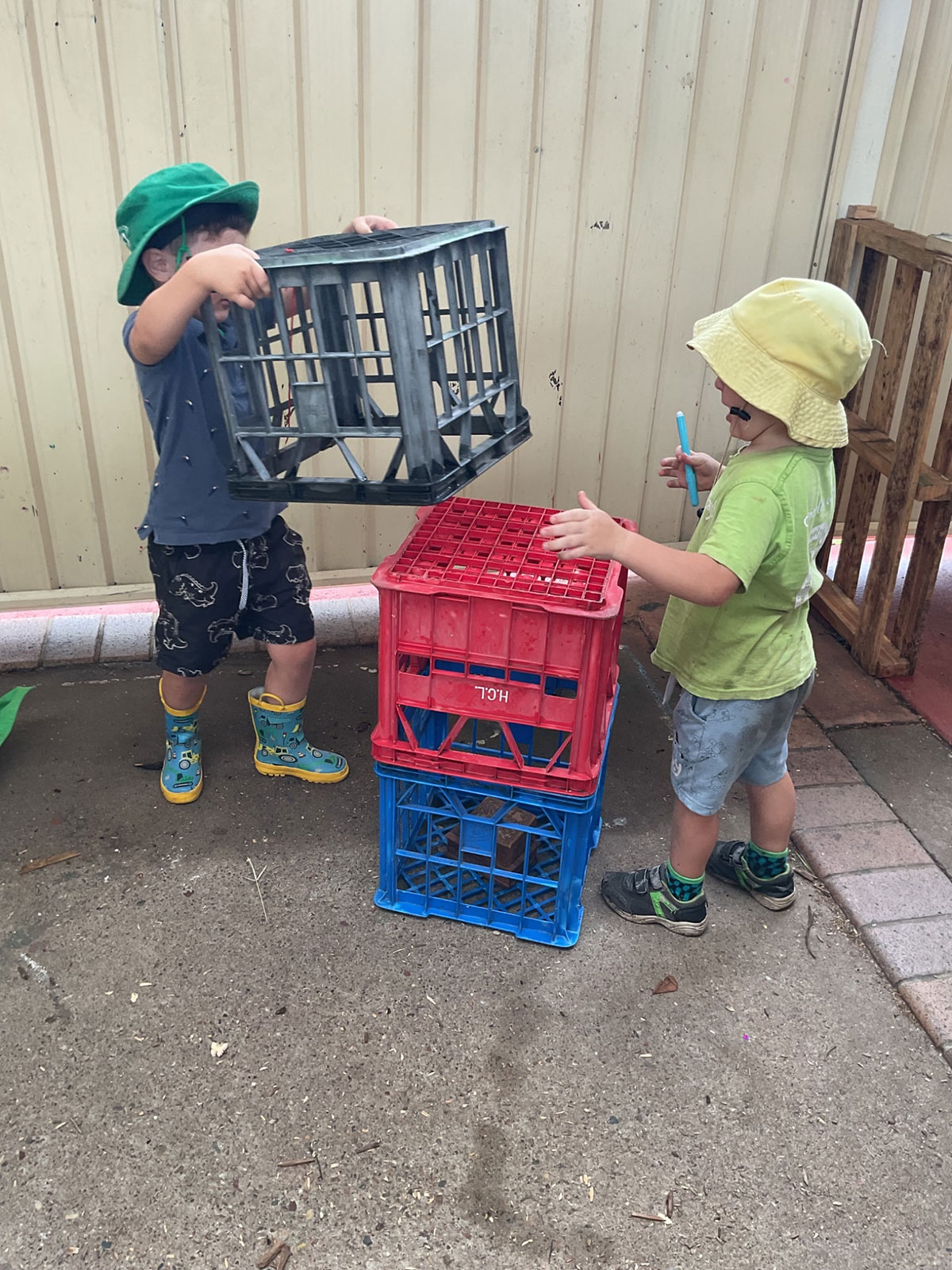 Two children are building a structure out of milk crates
